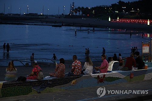 People dip their feet in seawater to cool off on a beach of the southern Jeju Island on July 1, 2025. (Yonhap)
