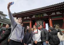 Tourists pose for photographs in front of the Senso-ji temple's Kaminari-mon gate in Tokyo's Asakusa area on Jan. 15, 2025. (Kyodo)